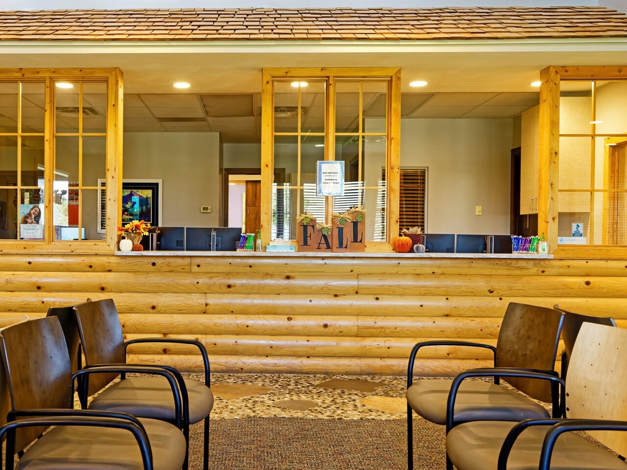 Wood-paneled reception area with fall-themed decorations on the counter. Several chairs are arranged in the waiting area; a person is behind the counter.