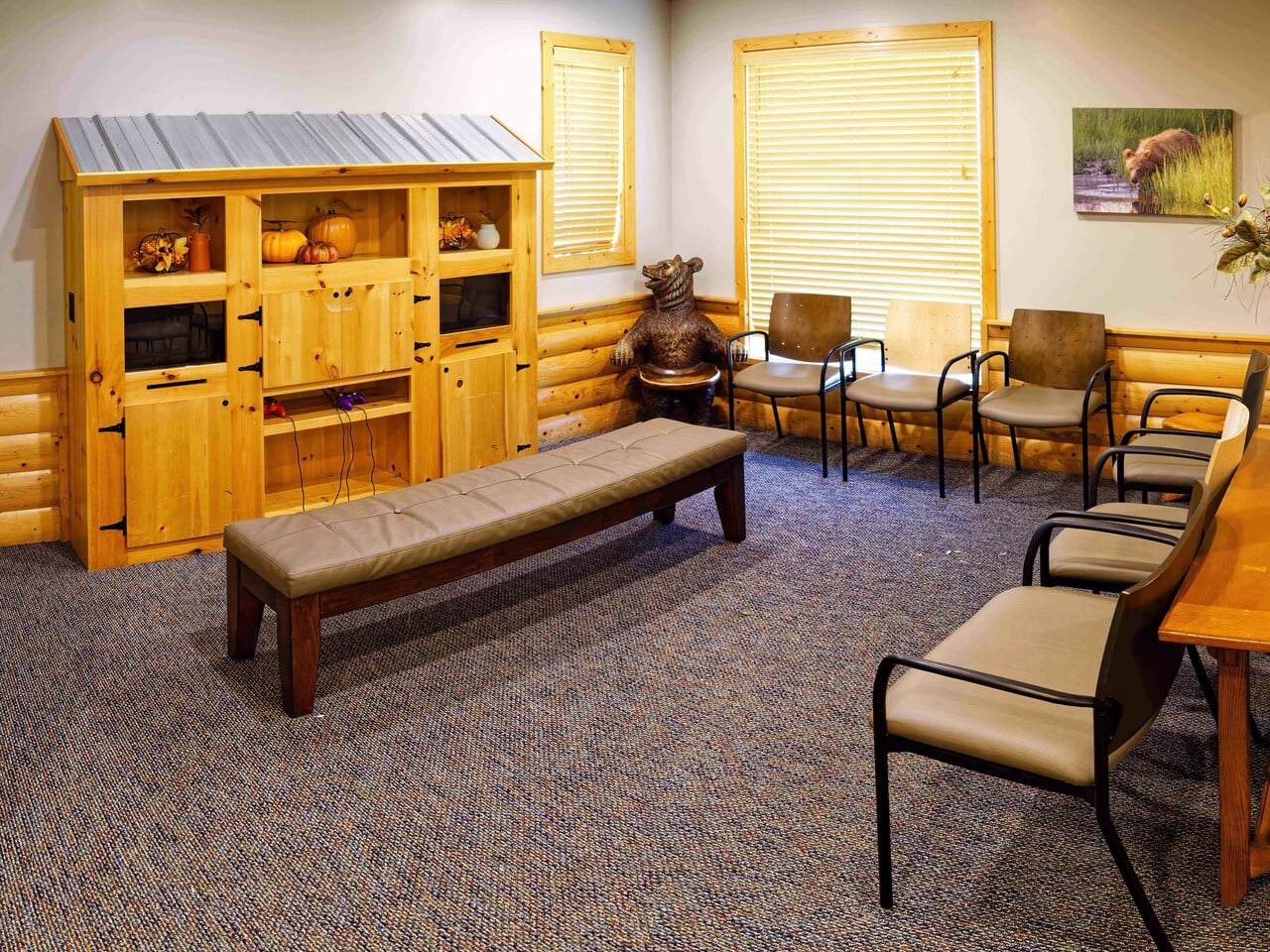 Cozy waiting room with rustic decor, wooden furniture, animal statue, and nature-themed artwork. Several chairs and a bench are neatly arranged.