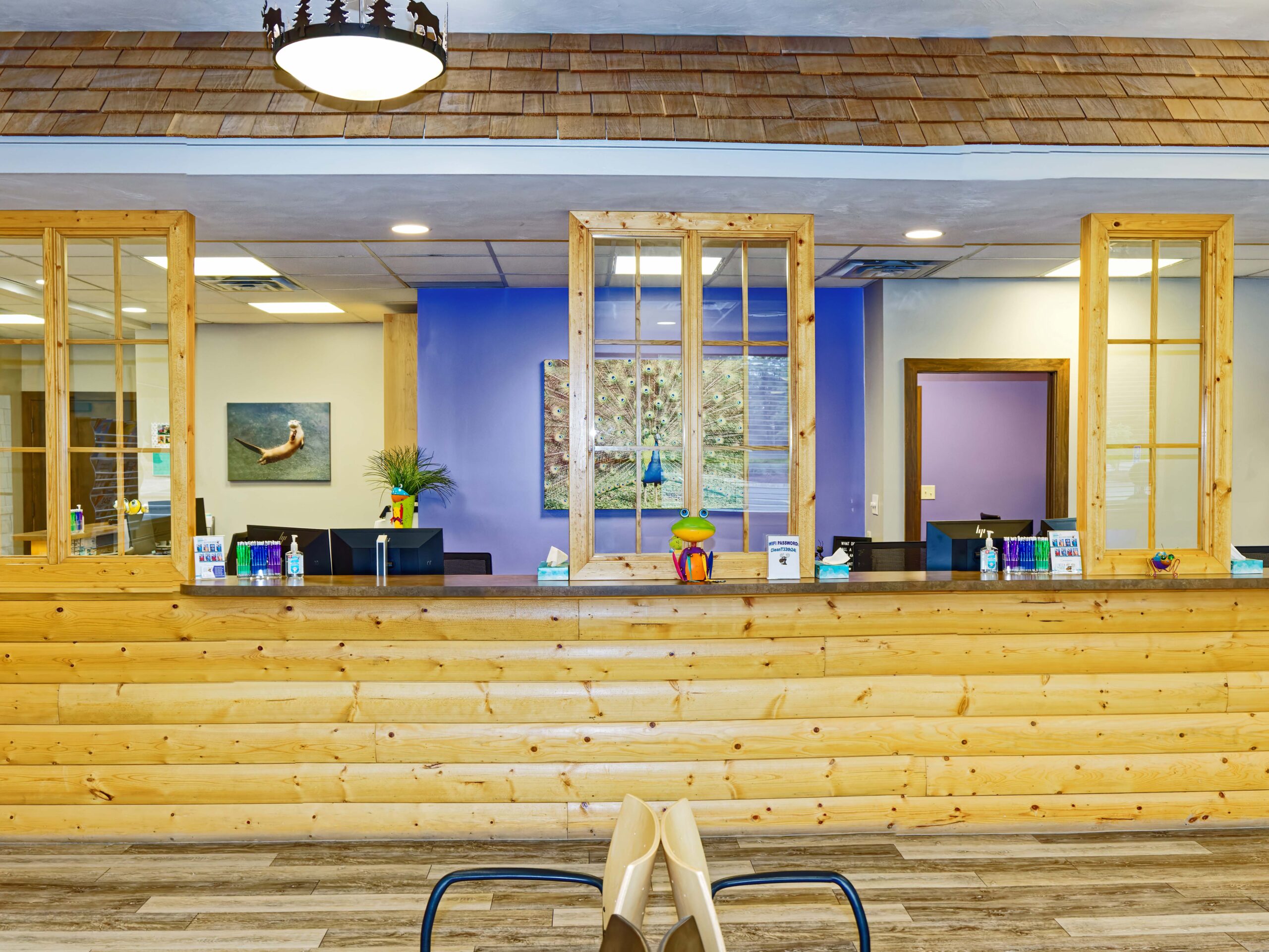 Reception area with wooden counter and decor. Bright paintings and toys create a welcoming environment. Casual seating in front enhances the inviting space.